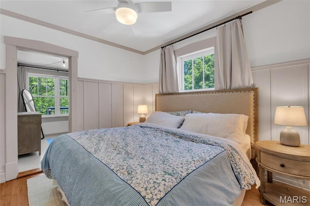 bedroom with a decorative wall, multiple windows, crown molding, wainscoting, and wood finished floors