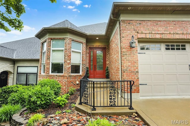 doorway to property featuring a garage, brick siding, roof with shingles, and driveway