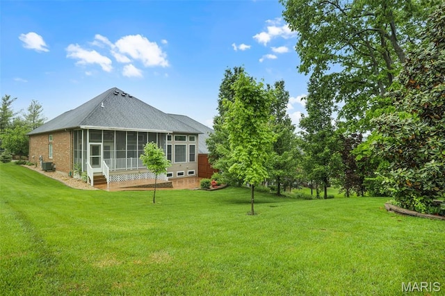 rear view of property with a sunroom, a yard, a shingled roof, and brick siding