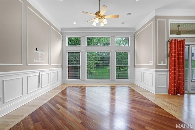 unfurnished living room with a decorative wall, crown molding, a ceiling fan, and wood finished floors