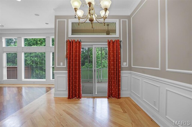 unfurnished dining area with a decorative wall, plenty of natural light, a chandelier, ornamental molding, and a wainscoted wall