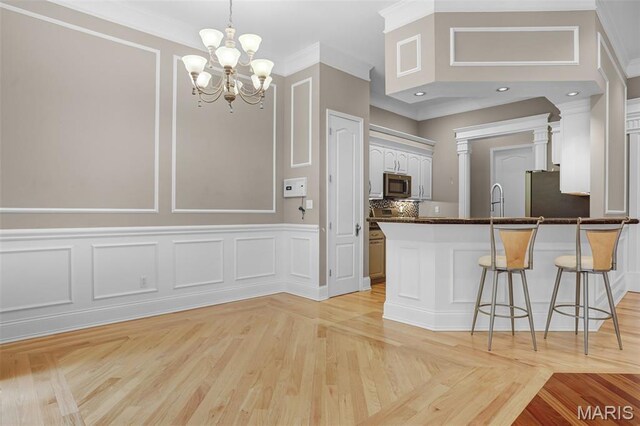 kitchen featuring stainless steel appliances, a decorative wall, a kitchen bar, white cabinetry, and a peninsula