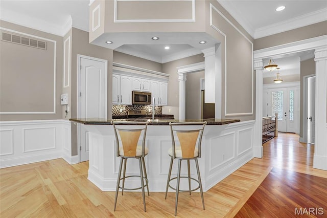 kitchen with appliances with stainless steel finishes, a breakfast bar, a peninsula, white cabinetry, and a decorative wall