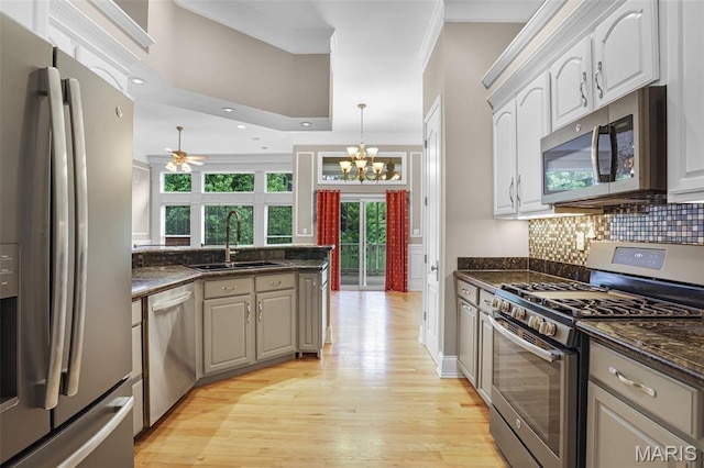 kitchen with stainless steel appliances, a sink, light wood-style flooring, backsplash, and ceiling fan