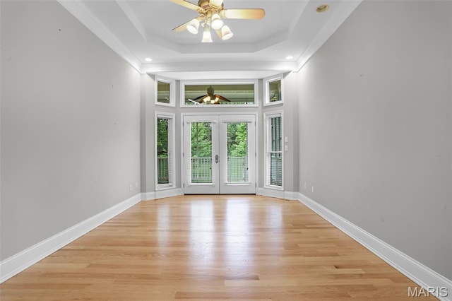 unfurnished room featuring a tray ceiling, light wood finished floors, french doors, ornamental molding, and baseboards