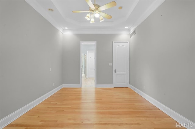 spare room with a tray ceiling, a ceiling fan, crown molding, light wood-style flooring, and baseboards