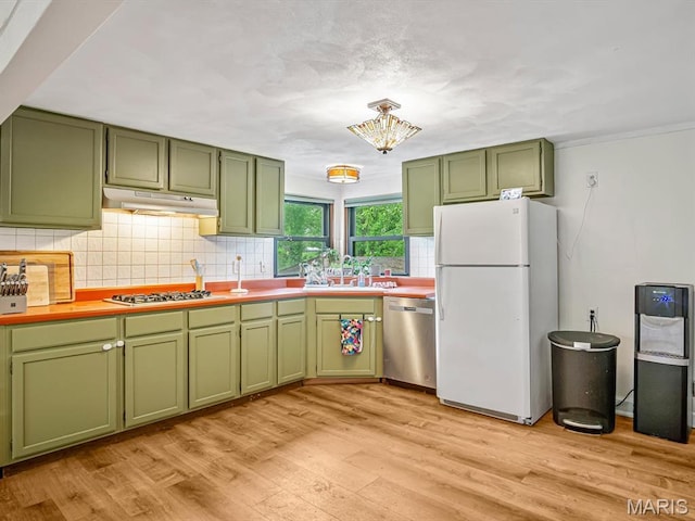 kitchen with green cabinets, appliances with stainless steel finishes, under cabinet range hood, decorative backsplash, and ornamental molding