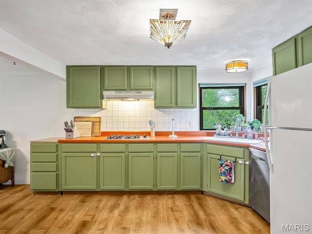 kitchen with freestanding refrigerator, green cabinets, dishwasher, under cabinet range hood, and a sink