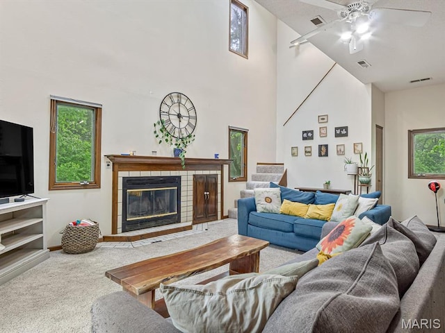 living area featuring carpet, ceiling fan, a fireplace, stairs, and a towering ceiling