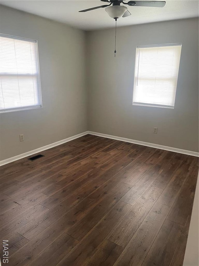 empty room featuring ceiling fan, plenty of natural light, dark wood-style flooring, and baseboards