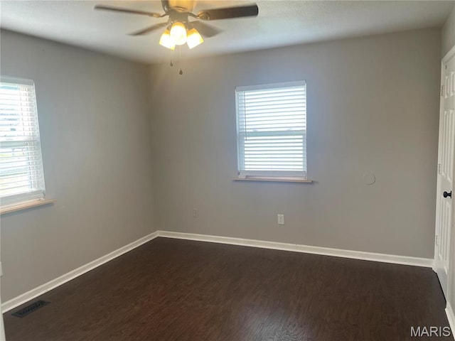 spare room with dark wood-style flooring, healthy amount of natural light, a ceiling fan, and baseboards