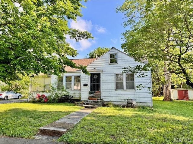 bungalow-style home featuring a front yard, a shingled roof, a shed, and an outdoor structure
