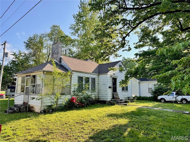 view of front of house featuring a front yard, a chimney, a sunroom, and a shingled roof