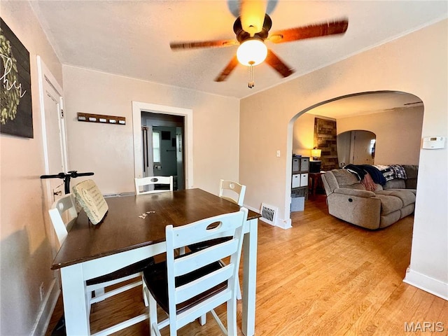 dining area featuring arched walkways, ceiling fan, light wood-type flooring, and baseboards