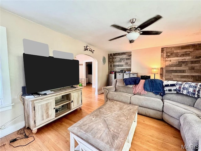 living room featuring arched walkways, a ceiling fan, light wood finished floors, and baseboards