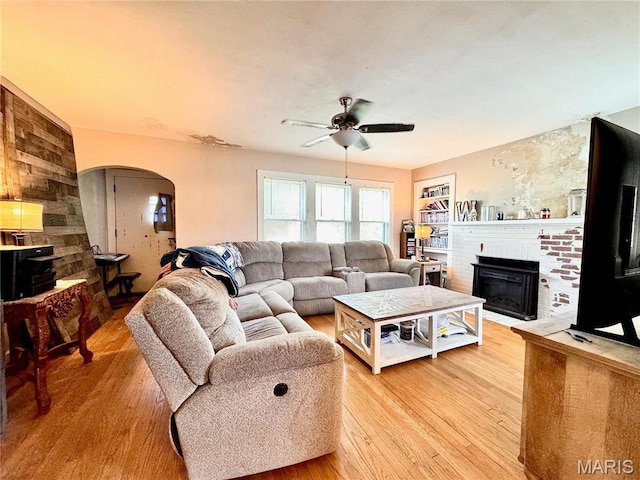 living area with arched walkways, light wood finished floors, ceiling fan, and a fireplace