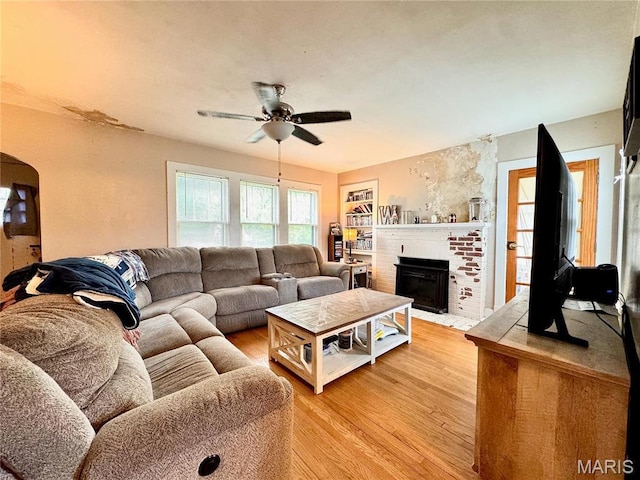 living room with light wood-style floors, a ceiling fan, a fireplace, and arched walkways