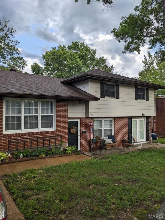 tri-level home with brick siding, a patio area, and a front lawn