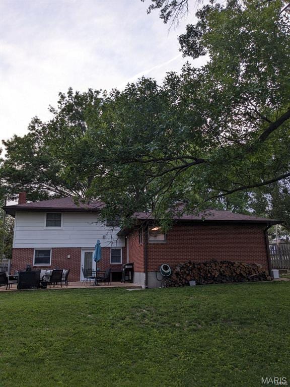 rear view of property with brick siding, a lawn, and a chimney