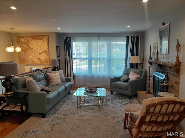 living area with wood finished floors, a chandelier, a stone fireplace, and recessed lighting