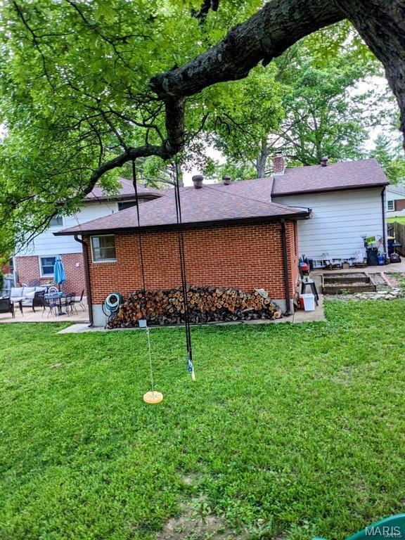 back of house with a chimney, a lawn, and brick siding