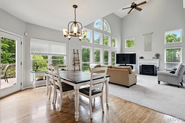 dining space with light wood-type flooring, ceiling fan, a chandelier, a fireplace, and high vaulted ceiling