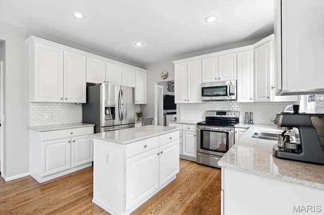 kitchen with appliances with stainless steel finishes, a center island, backsplash, white cabinets, and light wood-type flooring