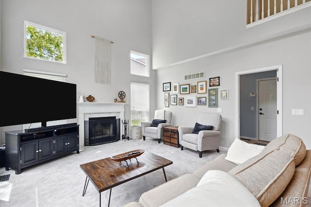 living area featuring a high ceiling, light carpet, and a fireplace with flush hearth
