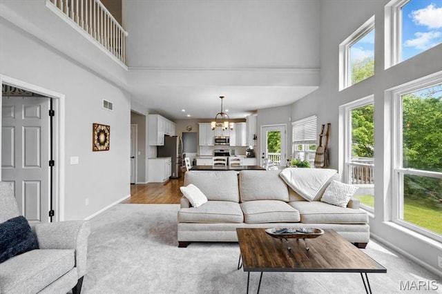 living area featuring a high ceiling, baseboards, light colored carpet, and a chandelier