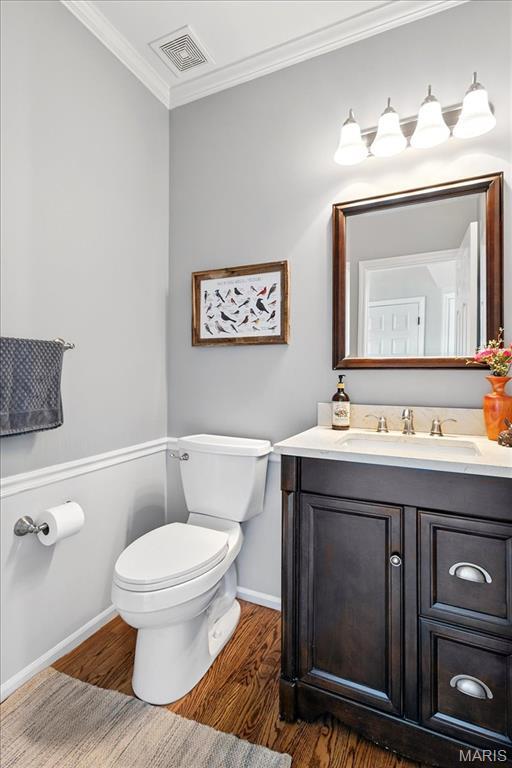 half bath featuring wood finished floors, baseboards, ornamental molding, toilet, and vanity