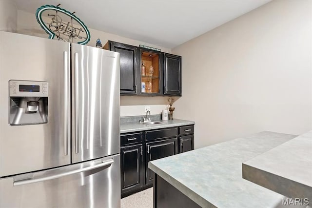 kitchen with stainless steel fridge, a sink, dark cabinets, and light countertops
