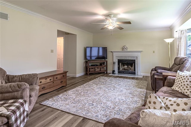 living area with ornamental molding, ceiling fan, wood finished floors, baseboards, and a fireplace