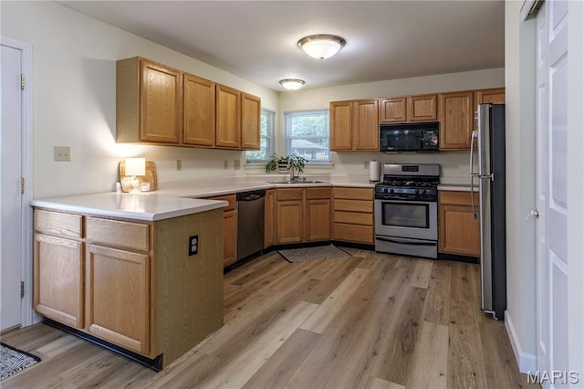 kitchen featuring appliances with stainless steel finishes, a sink, a peninsula, light wood finished floors, and light countertops