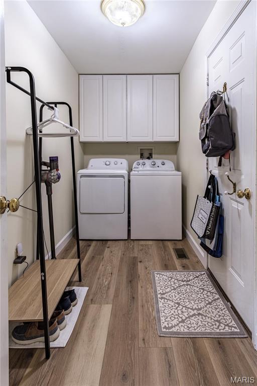 clothes washing area with cabinet space, washer and clothes dryer, light wood finished floors, and baseboards