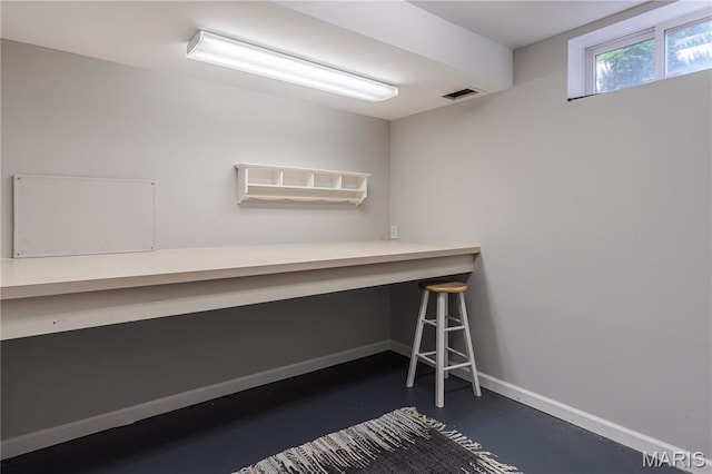 unfurnished office featuring finished concrete floors, built in desk, and baseboards