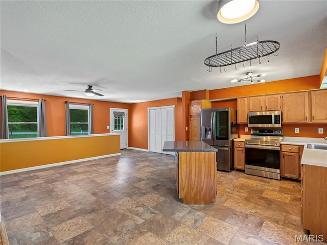 kitchen featuring appliances with stainless steel finishes, baseboards, a kitchen island, light stone finish floors, and ceiling fan
