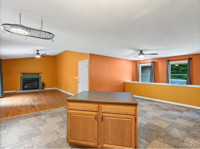 kitchen with a ceiling fan, stone finish flooring, baseboards, a center island, and dark countertops