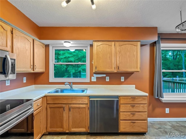 kitchen featuring stainless steel appliances, a sink, light countertops, a textured ceiling, and baseboards