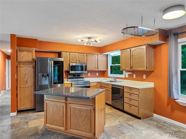 kitchen with appliances with stainless steel finishes, a sink, stone finish floors, baseboards, and a center island