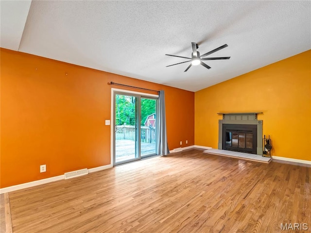 unfurnished living room featuring vaulted ceiling, a ceiling fan, wood finished floors, a textured ceiling, and a glass covered fireplace
