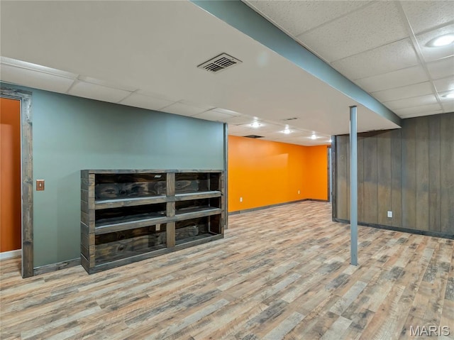 finished basement featuring a drop ceiling, wood finished floors, baseboards, and wooden walls