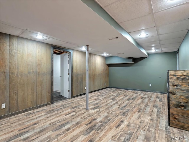 finished basement with a drop ceiling, wooden walls, wood finished floors, baseboards, and recessed lighting