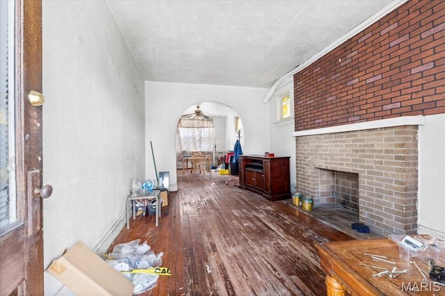 living area with hardwood / wood-style floors, a ceiling fan, arched walkways, and a brick fireplace