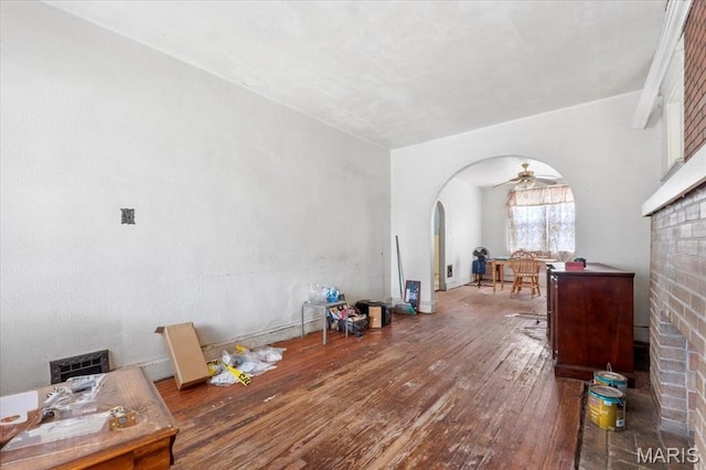 living area featuring arched walkways, hardwood / wood-style floors, a brick fireplace, and a ceiling fan