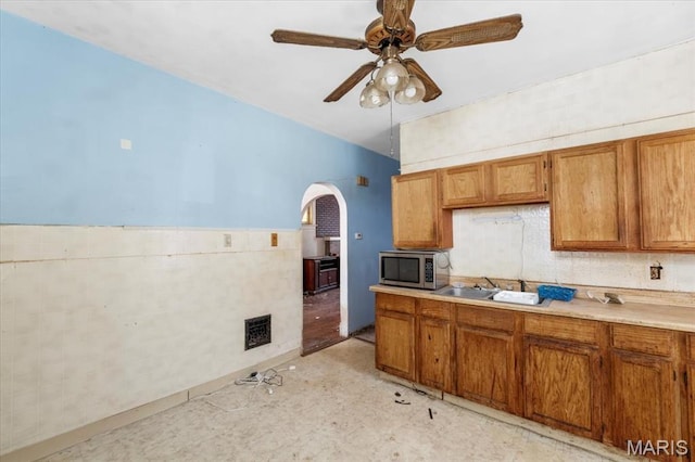 kitchen with stainless steel microwave, arched walkways, a sink, and brown cabinetry