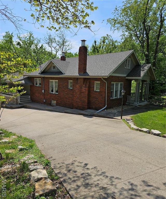 rear view of house featuring brick siding, a chimney, and a shingled roof
