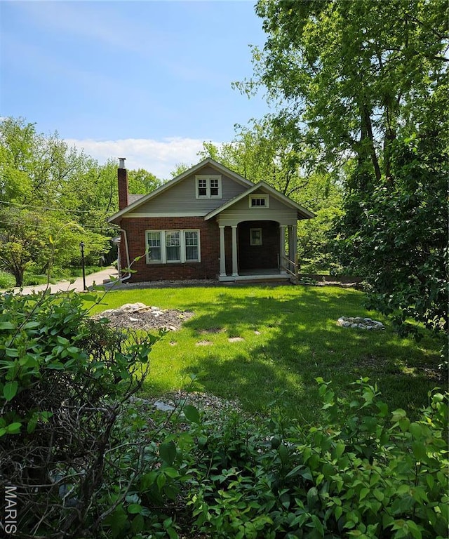 view of front of house with a chimney, a front lawn, brick siding, and a porch