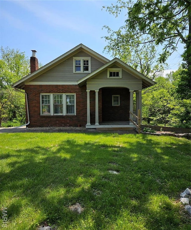 view of front of house featuring brick siding, a porch, a chimney, and a front yard