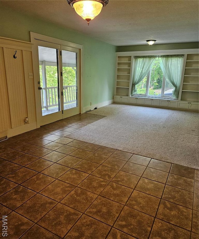 empty room with built in features, dark colored carpet, baseboards, dark tile patterned flooring, and a textured ceiling