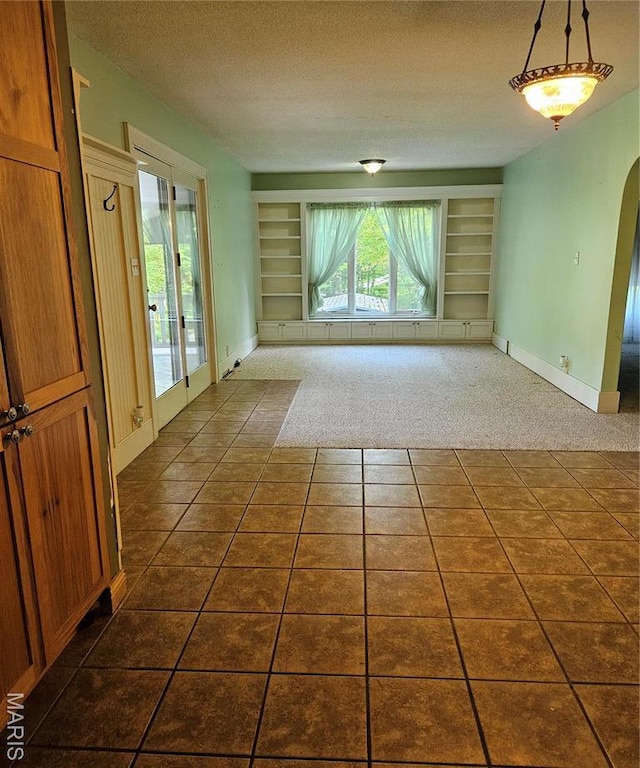 spare room with built in shelves, dark carpet, arched walkways, a textured ceiling, and baseboards